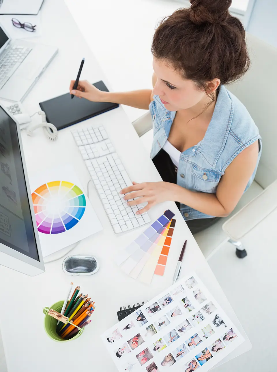 A young woman working on her pc while drawing on a tablet with her right hand and analyzing color palettes