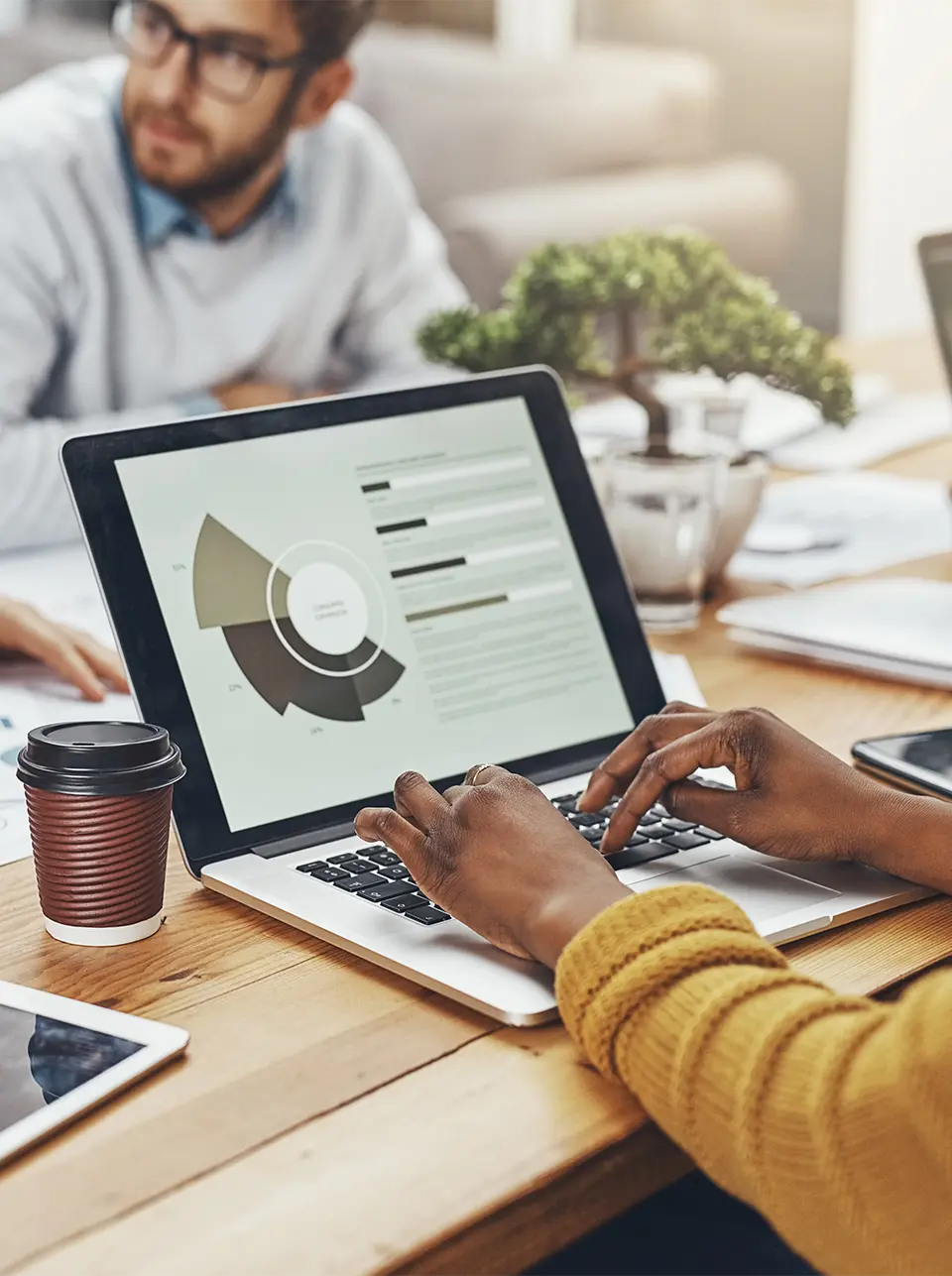 An employee focused on creating a pie chart, while another employee wearing glasses works diligently in the background, showcasing teamwork and productivity.